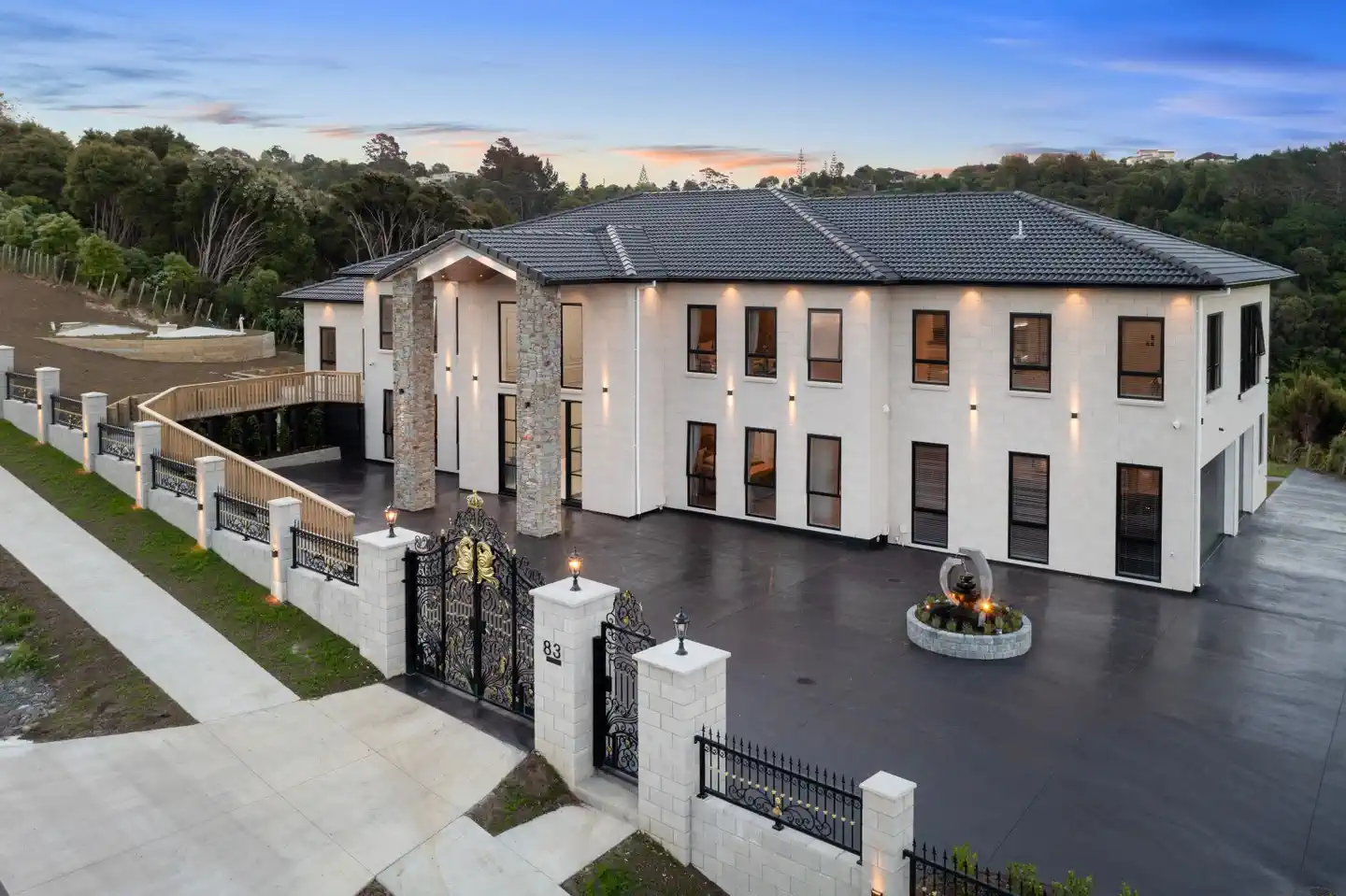 Large modern two-story house with stone pillars, decorative black gate, and driveway at dusk.