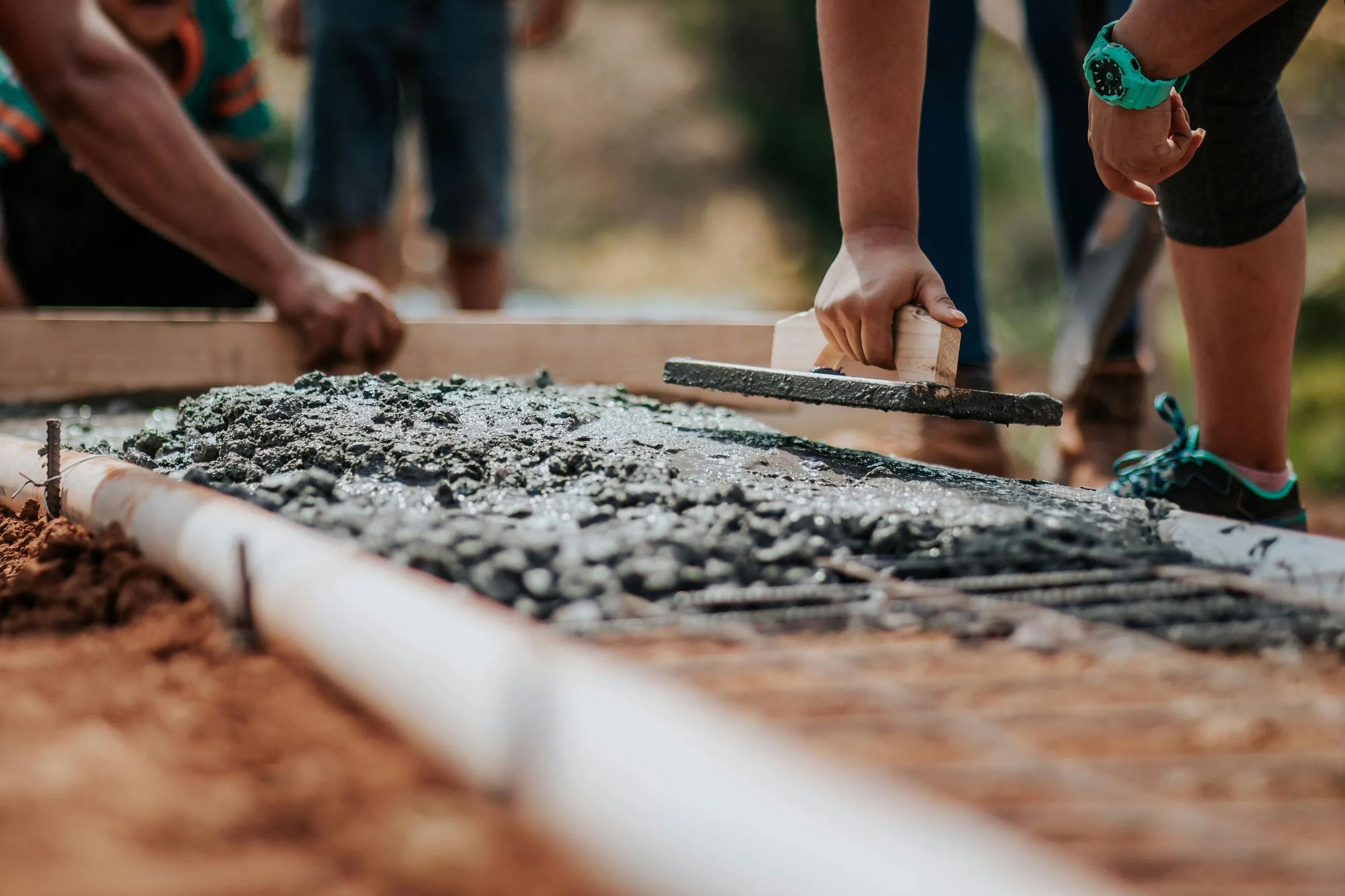 Close-up of two people smoothing freshly poured concrete with trowels on a construction site.