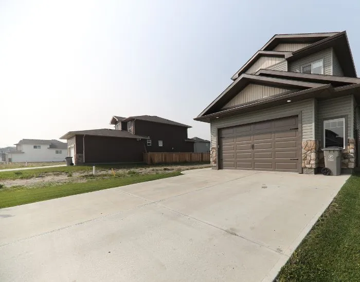 Modern two-story house with a large concrete driveway and a closed garage door.